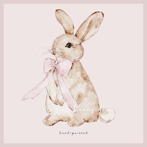 May include: A watercolor painting of a brown rabbit wearing a pink bow. The rabbit is sitting on a light pink background. The text "hand-painted" is written below the rabbit.