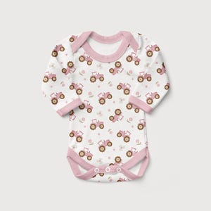 May include: White baby bodysuit with a pink tractor pattern. The long-sleeved onesie features a pink trim around the neckline, sleeves, and leg openings. The tractor design includes pink tractors and small floral accents.
