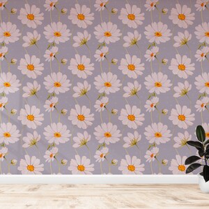 May include: A room with a light purple wall covered in a white daisy pattern. A potted plant with dark green leaves sits on the wooden floor.
