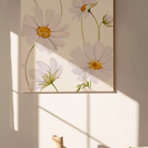 May include: A white canvas with a watercolor painting of white daisies with yellow centers. The daisies are arranged in a pattern on the canvas. The canvas is hanging on a white wall.