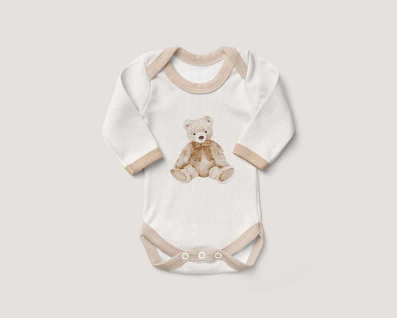 May include: White long-sleeve baby onesie with a brown teddy bear illustration on the front. The onesie has a beige trim around the neckline and snaps at the bottom.