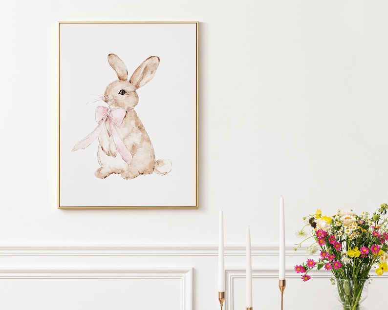 May include: A watercolor painting of a brown rabbit with a pink bow. The rabbit is sitting on a white background.