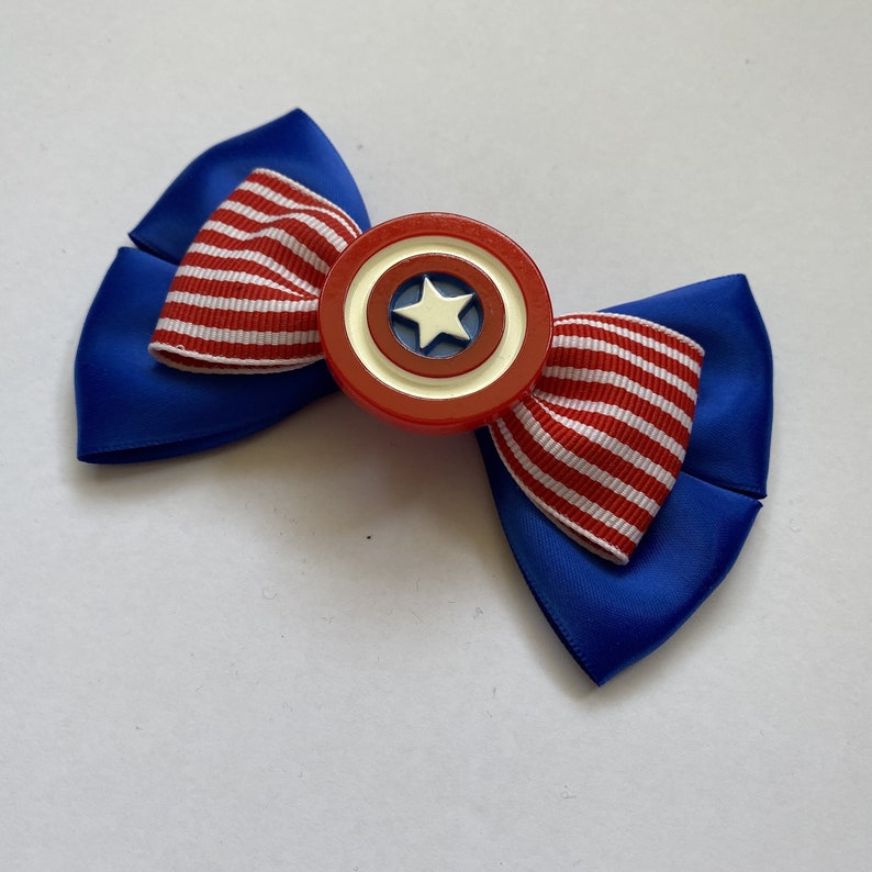 May include: A blue and red bow with a white star on a red, white, and blue circle in the center. The circle is a replica of Captain America's shield.