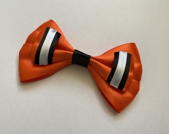 May include: A vibrant orange bow tie with black and silver accents. The bow tie is made of a satin-like material and features a black center band. The ends of the bow tie have a silver stripe bordered by black stripes.