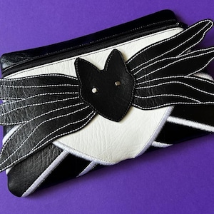 May include: Black and white leather clutch with a bat design. The bat has white stitching and a black leather nose.