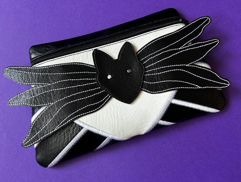 May include: Black and white leather clutch with a bat design. The bat has white stitching and a black leather nose.