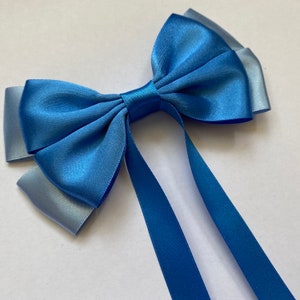 Op de afbeelding: Een blauwe satijnen strik met twee lange linten. De strik is gemaakt van twee tinten blauw, een donkerblauw en een lichtblauw.