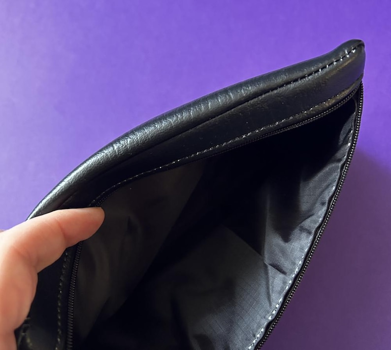 May include: A black leather zippered pouch with a black fabric lining. The pouch is open and the lining is visible.