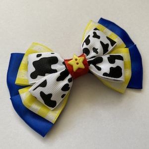 Pu&ograve; includere: Un fiocco giallo, bianco e blu con un nastro a stampa di mucca bianco e nero e un bottone rosso con una stella gialla.