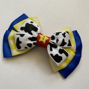 Pu&ograve; includere: Un fiocco blu, giallo e bianco con stampa di mucca e un bottone a stella rosso e giallo.