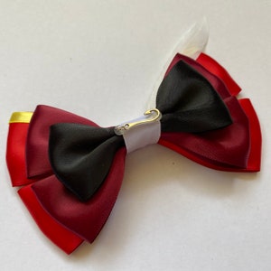 Puede incluir: Un lazo rojo, blanco y negro con un gancho y cierre de bucle plateado. El lazo está hecho de cinta de satén.