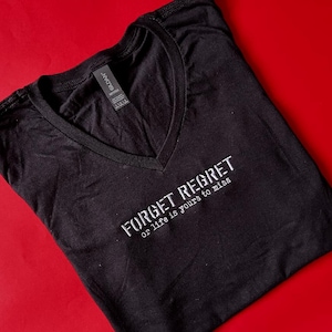 May include: Black v-neck t-shirt with the text "Forget Regret or life is yours to miss" embroidered in white.