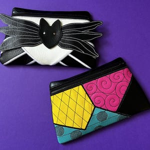 May include: Two black zippered pouches with different designs. The first pouch has a black bat with white stitching and a white background. The second pouch has a patchwork design with yellow, pink, blue, and black fabric.