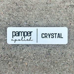 以下が含まれることがあります： 「pamper xpolish」と「CRYSTAL」という黒い文字が書かれた白い長方形のステッカーです。