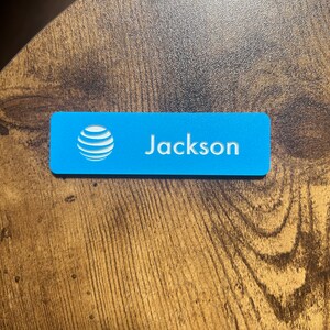 以下が含まれることがあります： 白いAT＆Tロゴと白い文字で「Jackson」と印刷された青い長方形のネームタグです。