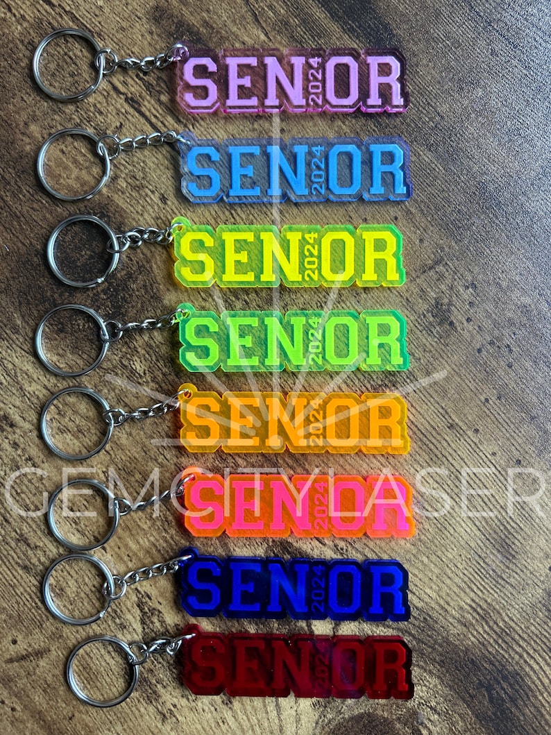 Pu&ograve; includere: Otto portachiavi con la scritta "Senior 2024" in diversi colori. I portachiavi sono realizzati in acrilico trasparente con il testo in grassetto, in bianco. I colori dei portachiavi sono rosa, blu, giallo, verde, arancione, rosso e viola.
