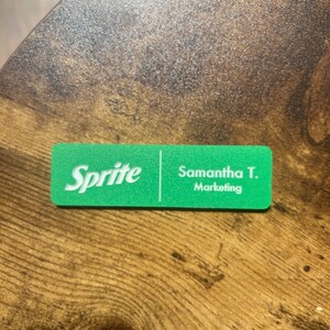 以下が含まれることがあります： 左側に「Sprite」の文字、右側に「Samantha T. Marketing」の文字が書かれた緑色の名札です。