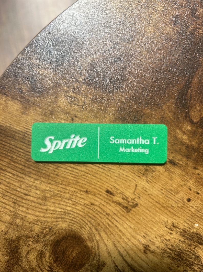 以下が含まれることがあります： 左側に「Sprite」の文字、右側に「Samantha T. Marketing」の文字が書かれた緑色の名札です。