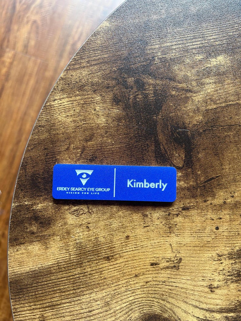 以下が含まれることがあります： 「Kimberly」というテキストと「Erdey Searcy Eye Group, Vision for Life」のロゴが書かれた青い名札