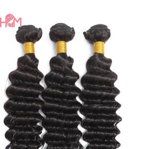 May include: Three bundles of black human hair extensions in a deep wave texture. The hair is tied with a gold elastic band at the top.