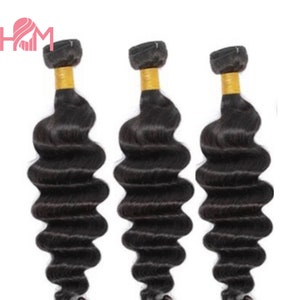May include: Three bundles of loose wave human hair extensions. The hair is black and has a natural wave pattern. The bundles are tied with a gold elastic band.