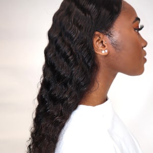 May include: A woman with long, dark, wavy hair. She is wearing a white shirt and has her hair styled in a side part.