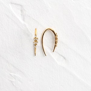 Puede incluir: Un par de pendientes de aro de oro con pequeñas piedras transparentes engastadas en el metal. Los pendientes son curvos y tienen un diseño sencillo.