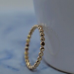 Op de afbeelding: Een gouden ring met kralen met een eenvoudig ontwerp. De ring is gemaakt van kleine, ronde kralen die gelijkmatig verdeeld zijn.