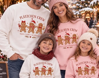 Op de afbeelding: Een gezin draagt bijpassende sweatshirts met de tekst PLÄTZCHEN CREW en drie peperkoekmannetjes. De volwassenen dragen witte en roze sweatshirts met mutsen, terwijl de kinderen ook bijpassende sweatshirts en mutsen dragen.