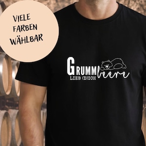 May include: Black t-shirt featuring white text and a bear graphic. The text says "Grummbeere Lieb (D)ich" with a sleeping bear illustration. A circular graphic in the upper left corner says "Viele Farben Wählbar".