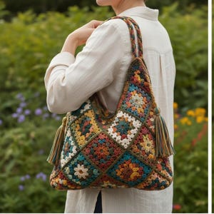 Può includere: Una colorata borsa tote all'uncinetto fatta a mano con un design patchwork. La borsa presenta quadrati nei toni del verde acqua, arancione, giallo e bianco, con un motivo floreale. Ha una tracolla intrecciata e nappe.