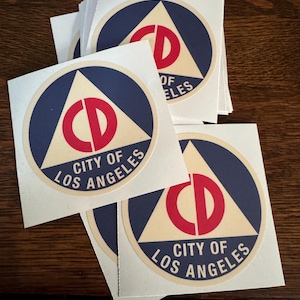May include: A stack of white stickers with a blue circle and a red and white triangle with the text "CITY OF LOS ANGELES" inside.