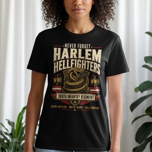 May include: A black short-sleeve t-shirt featuring a graphic design with the text NEVER FORGET HARLEM HELLFIGHTERS, 369TH INFANTRY REGIMENT, WWI, WWII, BLACK RATTLERS, MEN OF BRONZE, and HELL-FIGHTERS, centered around an illustration of a coiled rattlesnake.