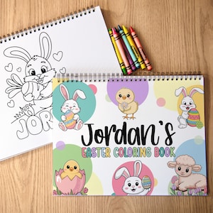 K&ouml;nnte beinhalten: Zwei Spiral-Malb&uuml;cher und Buntstifte auf einer Holzoberfl&auml;che. Ein Buch zeigt eine Schwarz-Wei&szlig;-Hasenillustration mit dem Namen "Jordan". Das andere Buch tr&auml;gt den Titel "Jordan's Easter Coloring Book" und enth&auml;lt farbenfrohe Illustrationen zum Thema Ostern.