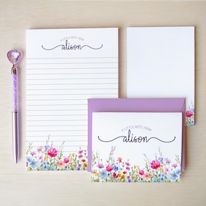 May include: A stationery set featuring a lined notepad and a note card with matching envelopes, all decorated with a colorful wildflower print at the bottom. The text A LITTLE NOTE FROM alison is printed on the notepad and card. A purple pen is included.