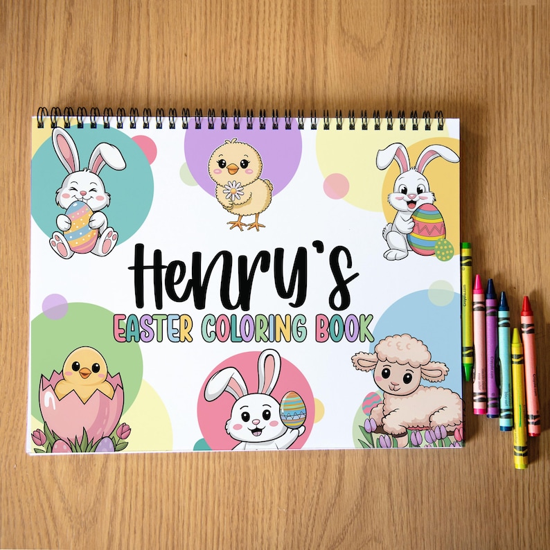 K&ouml;nnte beinhalten: Ein Spiral-Malbuch mit dem Text "Henry's Easter Coloring Book" und Illustrationen von Osterhasen, K&uuml;ken und einem Lamm. Buntstifte in verschiedenen Farben liegen auf der Holzoberfl&auml;che neben dem Buch.