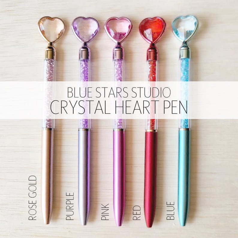 A collection of five colorful heart-shaped pens with glittery centers, arranged on a wooden surface.