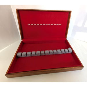 May include: A wooden silverware storage box with a red velvet interior. The box has two rows of gray slots for holding utensils. The exterior is a warm brown color.