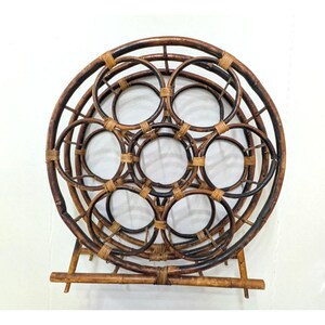 May include: A circular brown bamboo wine rack featuring a honeycomb pattern of seven interconnected circular bottle holders. The structure is reinforced with light tan woven bindings and supported by a horizontal bamboo base stand.