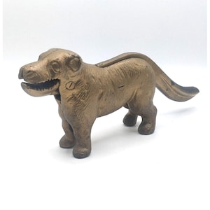 May include: A gold-colored cast iron dog nutcracker with a hinged jaw and a long tail. The dog is standing on all four legs.