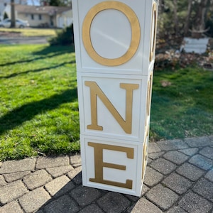 May include: White wooden blocks stacked to spell "ONE" with gold letters. The blocks are on a gray brick surface.