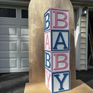 May include: A large wooden block tower spelling out "BABY" in pink and blue letters. The blocks are stacked on a wooden base.