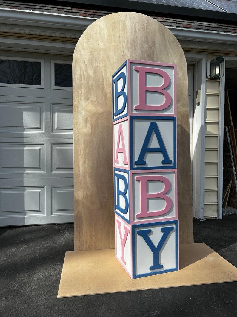 May include: A large wooden block tower spelling out "BABY" in pink and blue letters. The blocks are stacked on a wooden base.