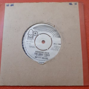 Op de afbeelding: Een zwart-witte 45-toeren vinylplaat met een wit label. Het label heeft een bellogo en de tekst "The Bell Martin-Coulter Music Ltd. BELL 13658 45 1974 Arranged by Phil Coulter BELL 1369 Produced by Bill Martin & Phil Coulter for Martin Coulter Enterprises Ltd. BRINGING BACK THE GOOD TIMES (B. Martin/P. Coulter) BAY CITY ROLLERS".