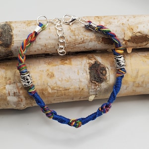 Peut inclure: Un bracelet fait à la main avec un cordon bleu tressé et des accents tressés colorés. Le bracelet comporte des perles en métal argenté et un fermoir réglable. Les sections tressées incorporent des fils aux couleurs de l'arc-en-ciel.