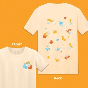 以下が含まれることがあります： 前面と背面にカラフルな折り紙猫のデザインが施されたクリーム色のTシャツ。前面には小さなデザインがあり、背面にはオレンジ、青、黄色の複数の折り紙の形と幾何学模様が表示されています。