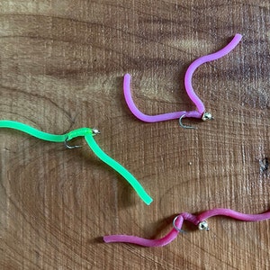 May include: Three fishing lures, one green, two pink, with gold beads and hooks.