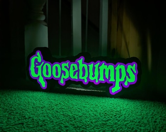 May include: A neon sign displaying the word "Goosebumps" in green with a purple outline, set against a black backdrop. The sign rests on a green carpet, with a dark background and a staircase in view.
