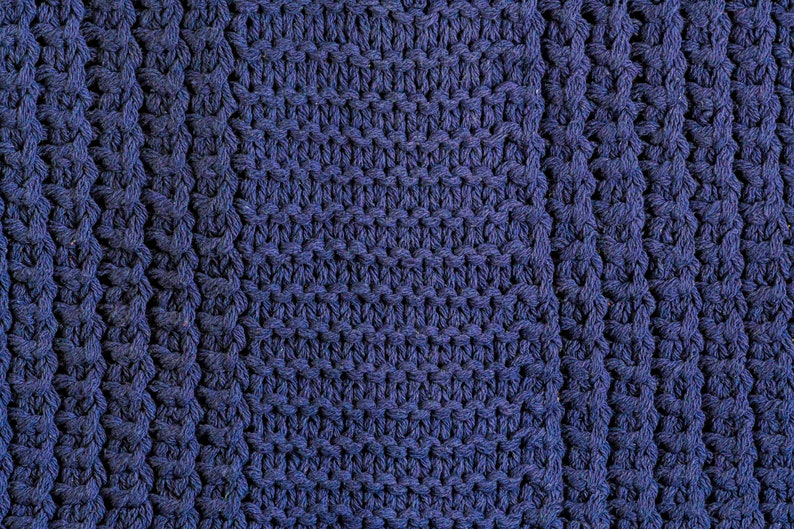 May include: Close-up of a blue knitted fabric with a textured pattern. The fabric is made of thick yarn and has a soft, cozy feel.