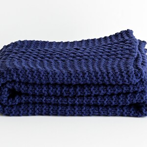 May include: A navy blue knitted throw blanket folded on a white surface.